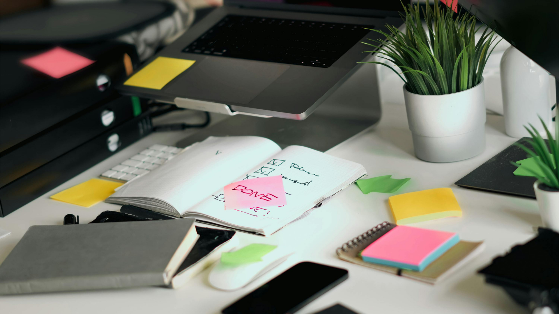 Desk with open notebook, smartphone, and office supplies on a white surface